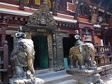 Kathmandu Patan Golden Temple 06 Elephants Guard Entrance From Inside Courtyard On either side of the entrance in the courtyard of the Golden Temple in Patan are two metal statues of elephants standing on tortoises. Between the elephants is the exquisite carved doorway with Buddha and the five Dhyani Buddhas on the arch above the entrance.